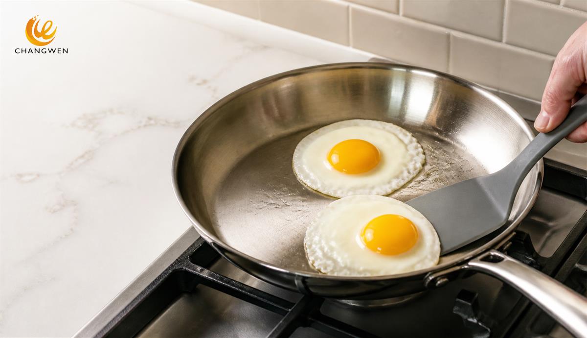 Two fried eggs releasing cleanly from a stainless steel frying pan